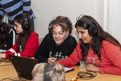 Jugendliche, die an einem PC sitzen und Kopfhörer aufhaben.