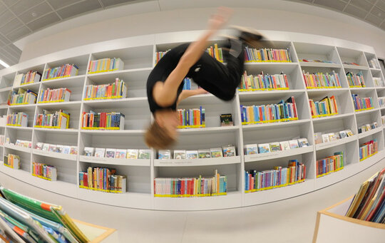Eine Person, die einen Salto vor einem Bücherregal macht.