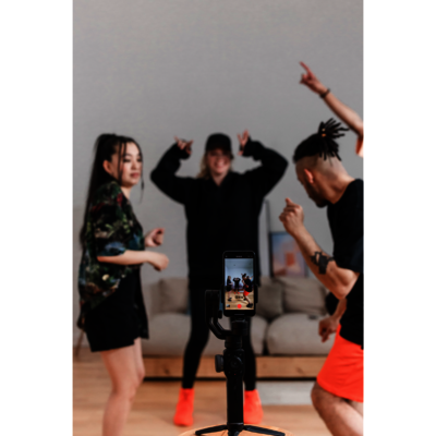 Drei Personen, die tanzen und dabei von einem Smartphone, welches auf einem Stativ befestigt ist, gefilmt werden.