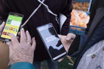 Eine Hand eines älteren Menschen mit einem Smartphone in der Hand, die neben einer Hand eines junge Menschen mit einem Smartphone in der Hand zu sehen ist.