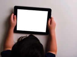 Ein Kind, das vor einem Tablet sitzt, welches es in den Händen hält.