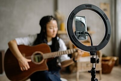 Eine Person, die sitzend Gitarre spielt und von einem Smartphone gefilmt wird.