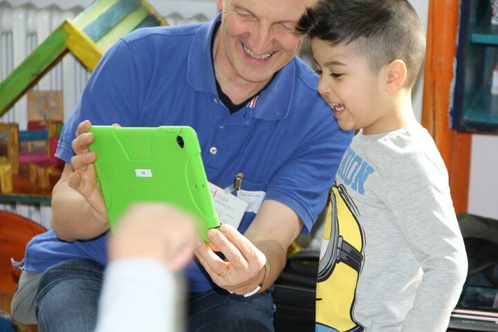 Eine erwachsene Person mit Tablet in den Händen, die einem Kind etwas auf dem Tablet zeigt