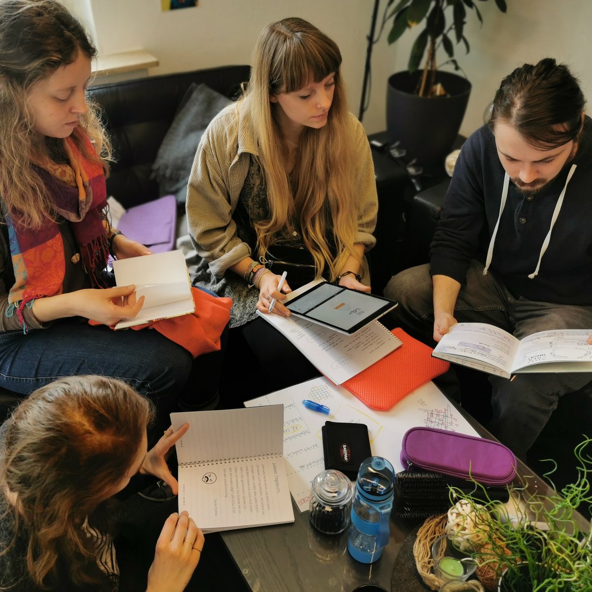Menschen, die um einen Tisch sitzen und Notzibücher und Tablets vor sich haben
