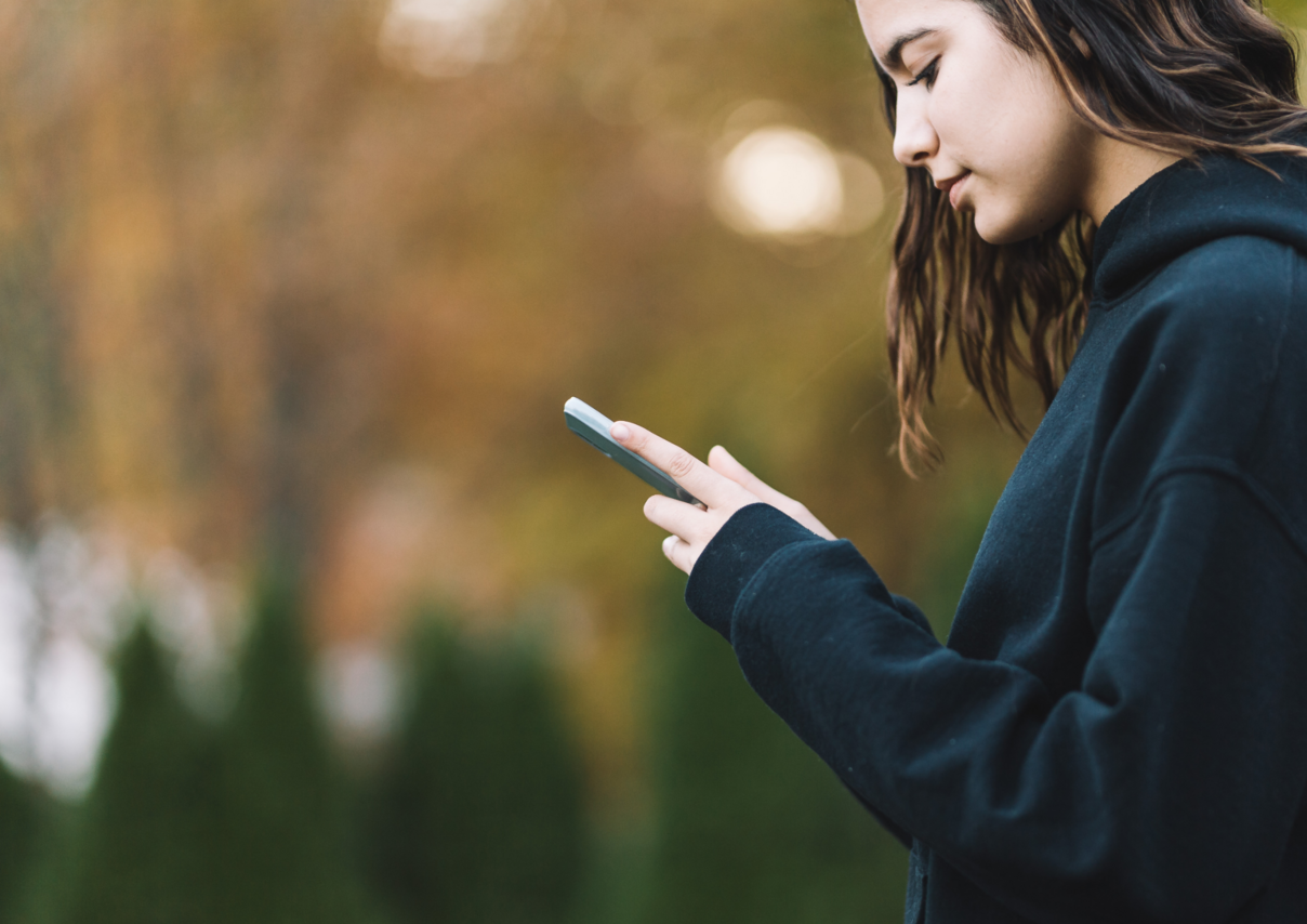 Eine junge Person, die ein Smartphone in den Händen hält.