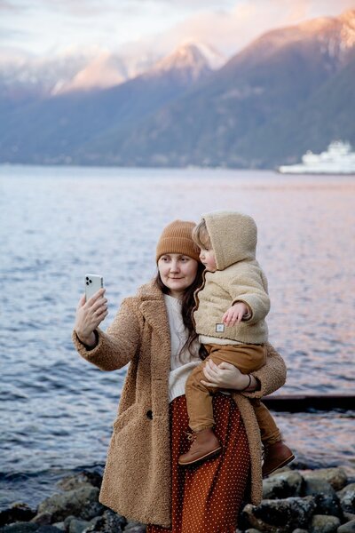 Eine erwachsene Person, die von sich und ihrem Kleinkind ein Foto mit dem Smartphone macht.
