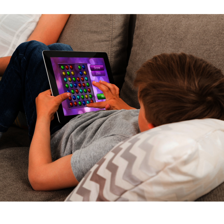 Ein Kind, das auf einem Sofa liegt und ein Spiel auf einem Tablet spielt.