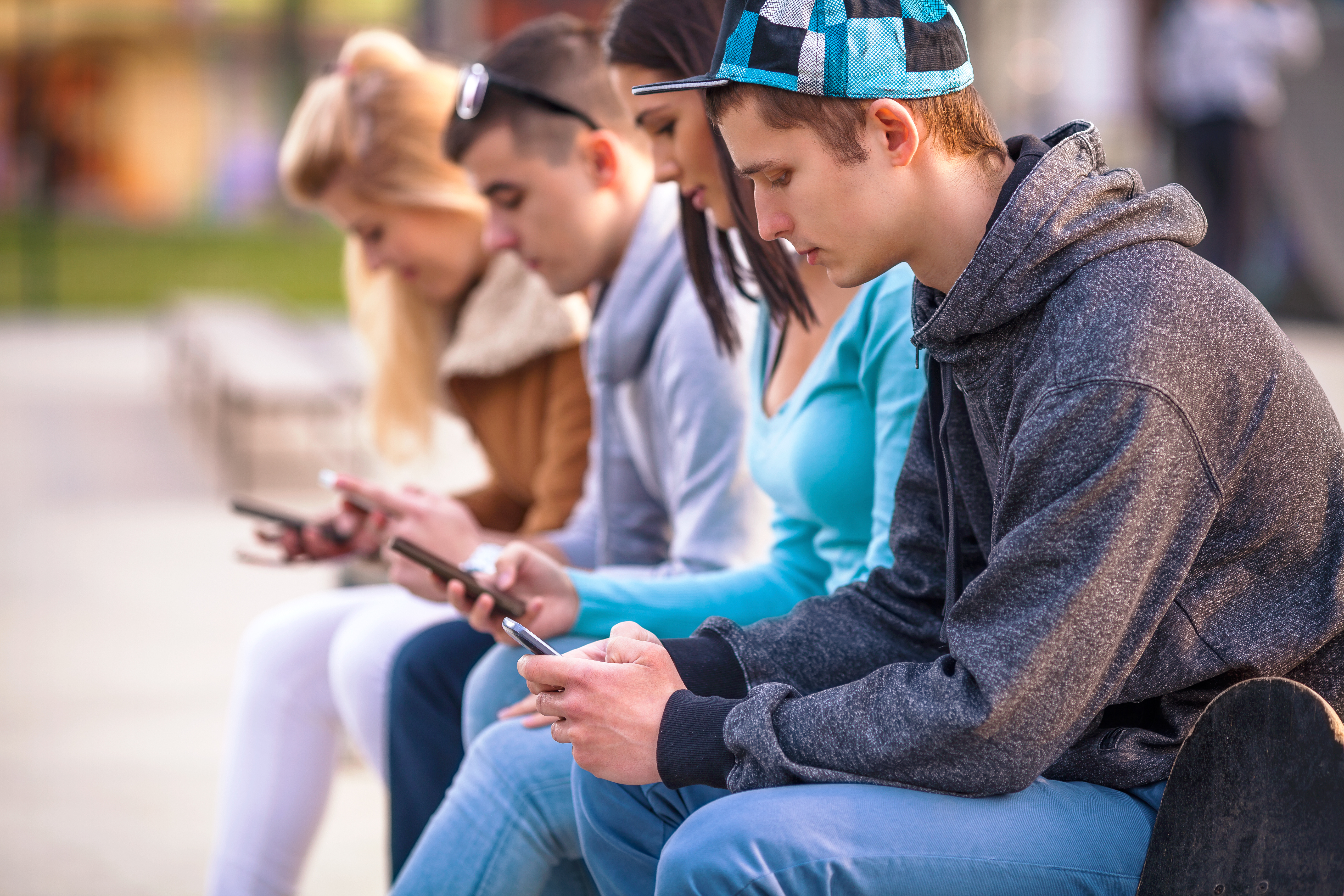 Eine Gruppe von Jugendlichen sitzt auf einer Bank im Park. Jeder schaut auf sein Smartphone. 