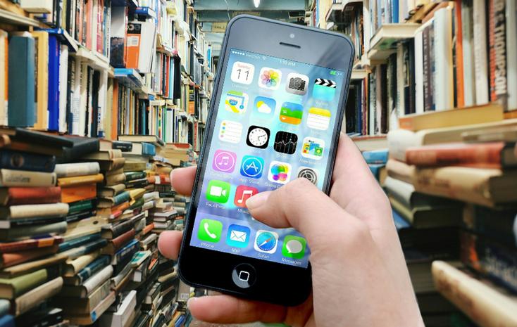 Hand hält Smartphone zwischen vollen Bücherregalen 