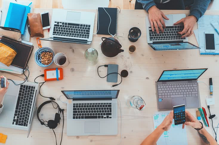 Gruppenarbeit: Draufsicht auf Arbeitstisch mit Laptops, Smartphones, Notizen etc.
