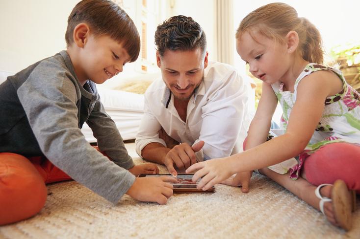 Ein Vater spielt mit seinen Kindern am Tablet.