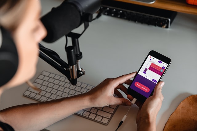 unsplash_Soundtrap.jpg Eine Person, die in ein Mikrofon spricht und ein Smartphone in den Händen hält.