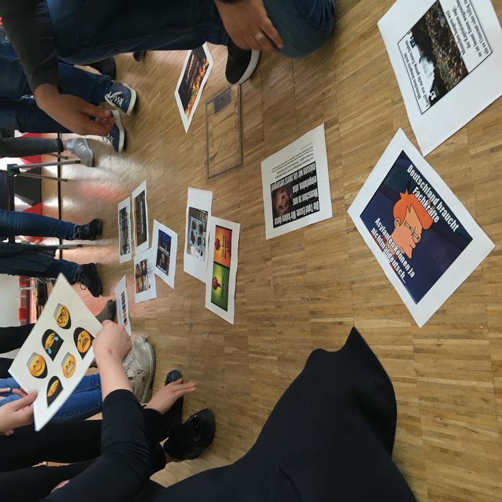 Heiko Wolf_Workshop_Hass im Netz.jpeg Memes, die auf Papier abgebildet sind und von Menschen in einem Workshop diskutiert werden