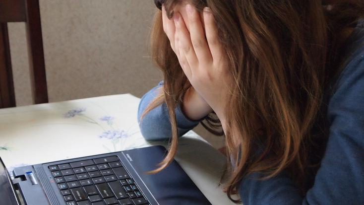 Kind vor Laptop vergräbt Gesicht in den Händen 