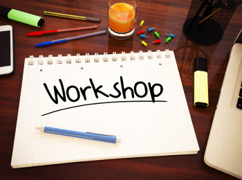 Ein Papier, Stifte und ein Laptop, die auf einem Tisch liegen. Auf dem Papier steht "Workshop". 