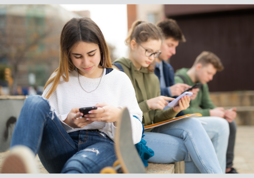 Junge Menschen, die draußen sitzen und ein Smartphone in den Händen halten, auf das sie schauen.