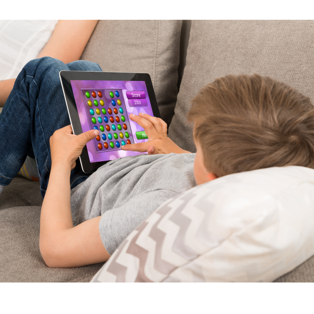 Ein Kind, das auf einem Sofa liegt und ein Spiel auf einem Tablet spielt. 